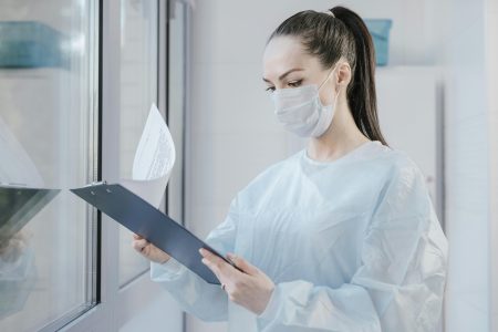 A female doctor in a mask examining patient's medical records in a hospital setting.